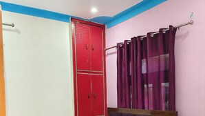 Ein Schlafzimmer mit einem Bett, einem roten Kleiderschrank, einem Deckenventilator und einem Vorhang.