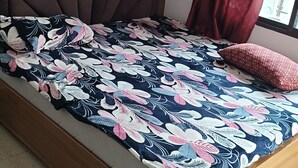 Ein Bett mit Blumenmuster auf der Tagesdecke, ein Holz-Kopfteil und ein Fenster mit Vorhängen.