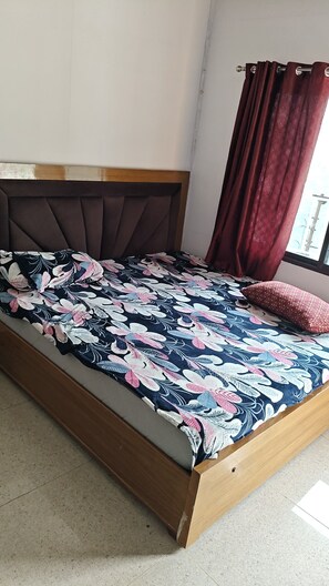 Una cama con colcha floral, cabecera de madera y ventana con cortinas.