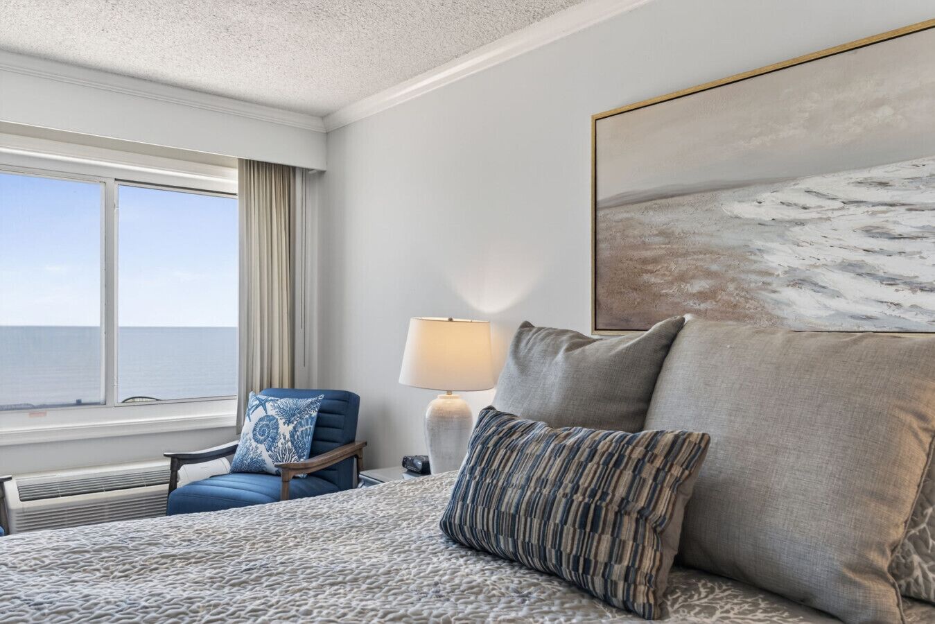 Une chambre d’hôtel avec un lit, une chaise, une lampe et un grand tableau.