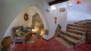A room with a stone fireplace, a wooden bench with cushions, a large rock archway, and a staircase with stone steps. - Altair Blue Villa - Private Jacuzzi and Views (Kalo Chorio)