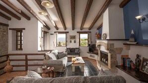 A rustic interior with exposed wooden beams, a stone fireplace, and a seating area with patterned cushions. - Altair Blue Villa - Private Jacuzzi and Views (Kalo Chorio)