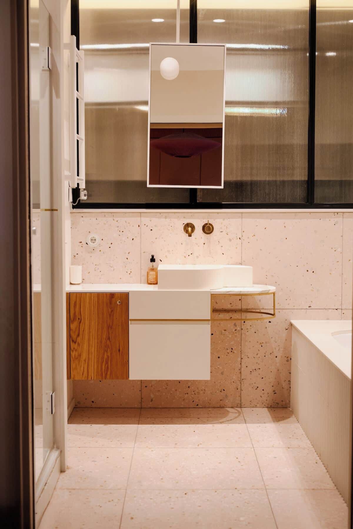 A modern bathroom with a white sink, wooden cabinet, and a mirror above the sink.