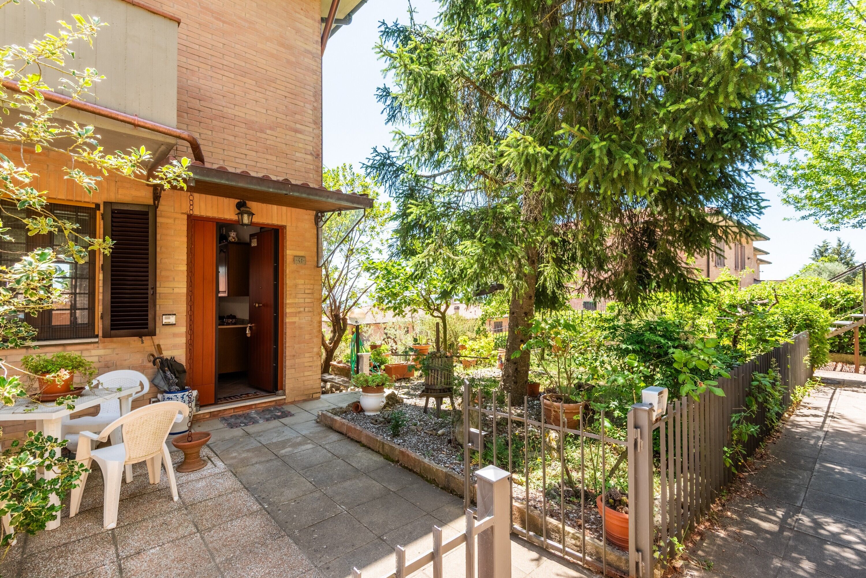 A courtyard with a table and chairs, potted plants, a wooden fence, and a tree.