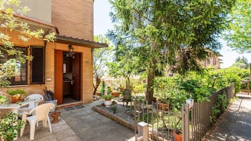 A courtyard with a table and chairs, potted plants, a wooden fence, and a tree.