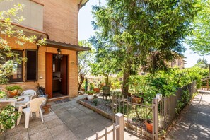 Un patio con una mesa y sillas, plantas en macetas, un cerco de madera y un árbol.