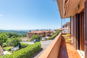 A residential balcony with a view of a residential area, a car parked in the driveway, and a clear sky.