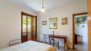 A bedroom with a bed, a desk, a chair, a radiator, and a door leading to a balcony.