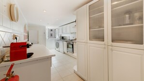 A modern kitchen with white cabinetry, a red kettle, a washing machine, and a stove. - Apartment 'Alfama Com Vista Rio' with Balcony, Wi-Fi and Air Conditioning (Lisboa)