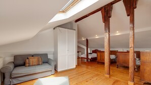 A loft-style room with a sloped ceiling, wooden beams, a grey sofa, a white wardrobe, and a wooden dining table. - Apartment 'Alfama Com Vista Rio' with Balcony, Wi-Fi and Air Conditioning (Lisboa)