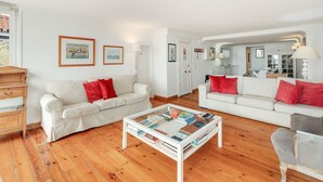 A living room with two white sofas, a coffee table with books, wooden flooring, and framed pictures on the walls. - Apartment 'Alfama Com Vista Rio' with Balcony, Wi-Fi and Air Conditioning (Lisboa)