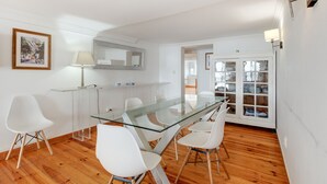 A modern dining area with a glass table, white chairs, and wooden flooring. - Apartment 'Alfama Com Vista Rio' with Balcony, Wi-Fi and Air Conditioning (Lisboa)