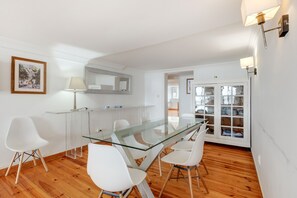Een moderne eetruimte met een glazen tafel, witte stoelen en een houten vloer.
