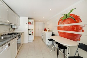 Een moderne keuken met witte kasten, een gasfornuis, een koelkast en een eethoek met een tafel en stoelen.