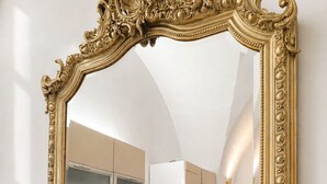 Eine Küche mit dunklen Schränken, einer Marmor-Spritzschutzwand und einem spiegelnden Rahmen in Gold.