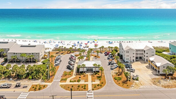 A beachfront hotel with a parking lot, a beach with umbrellas, and ocean views. - Sea Charm | Close to Beach | Golf Cart (LSV) | Community Pool (Santa Rosa Beach)