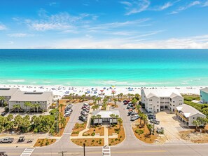 A beachfront hotel with a parking lot, a beach with umbrellas, and ocean views. - Sea Charm | Close to Beach | Golf Cart (LSV) | Community Pool (Santa Rosa Beach)