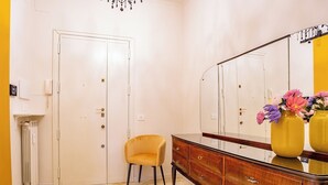 Ein Zimmer mit Marmorboden, einem Holzkoffer, einem Spiegel, einem gelben Stuhl und einer Tür.