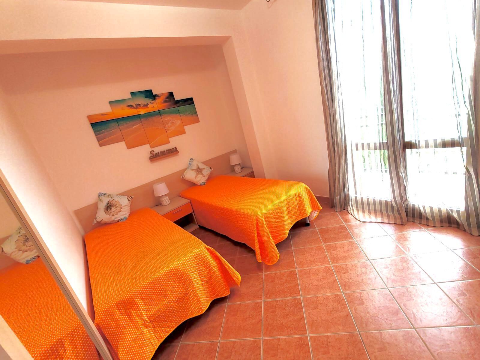 A room with two beds, a painting on the wall, and a window with curtains.