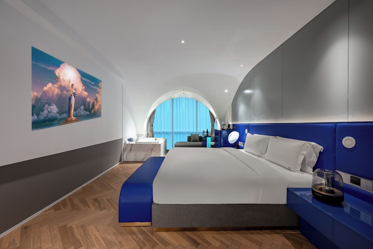 A modern bedroom with a large bed, a vanity, and a painting of a figure with a light.
