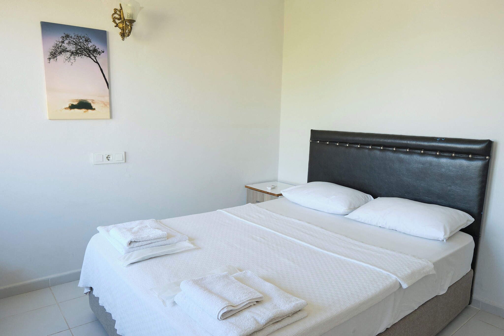 A hotel room with a bed, white linens, a nightstand, a lamp, and a wall-mounted picture.