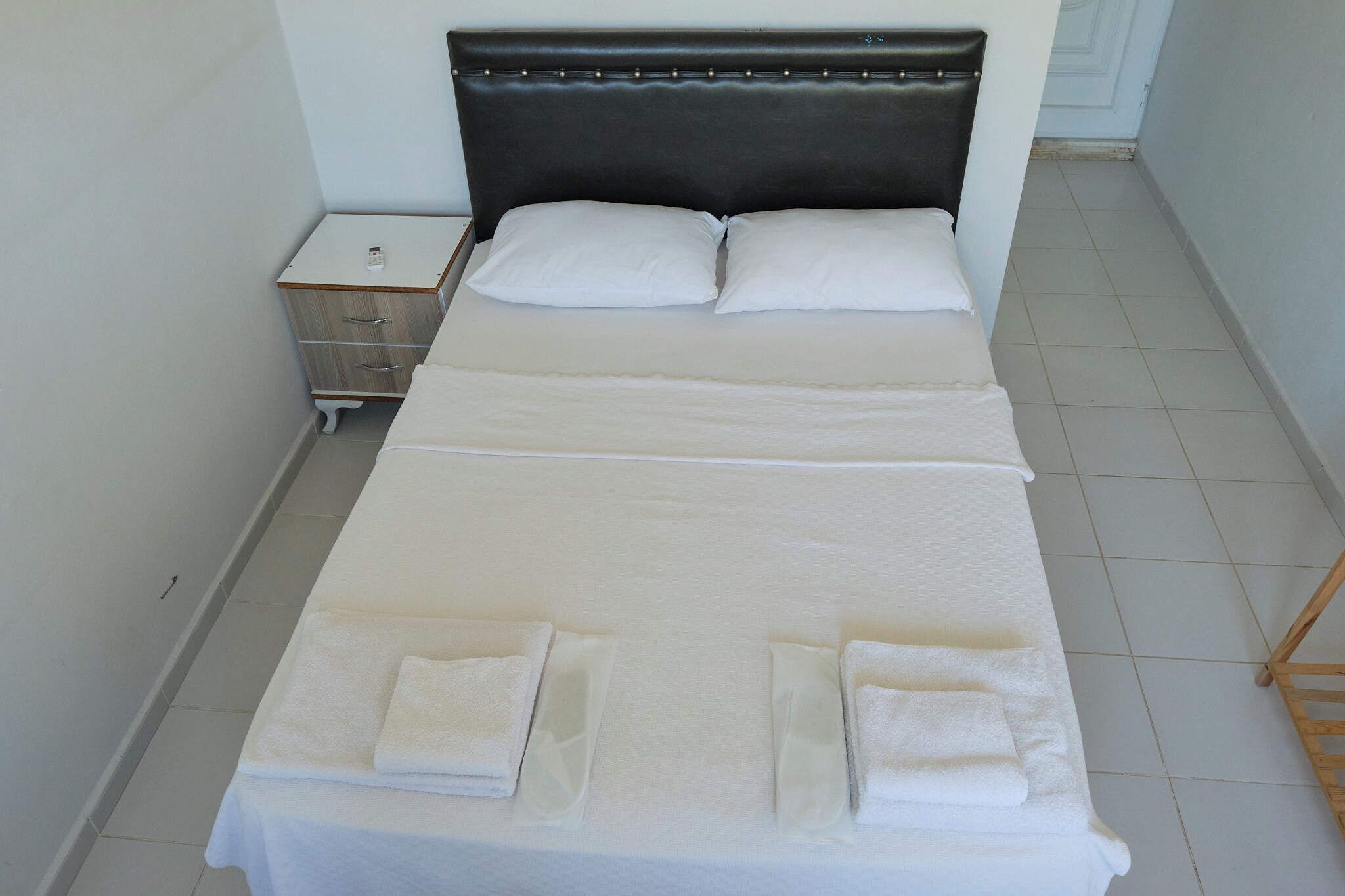 A neatly made bed with white linens and pillows, a bedside table with a lamp, and a wooden nightstand.