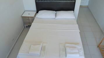 A neatly made bed with white linens and pillows, a bedside table with a lamp, and a wooden nightstand.