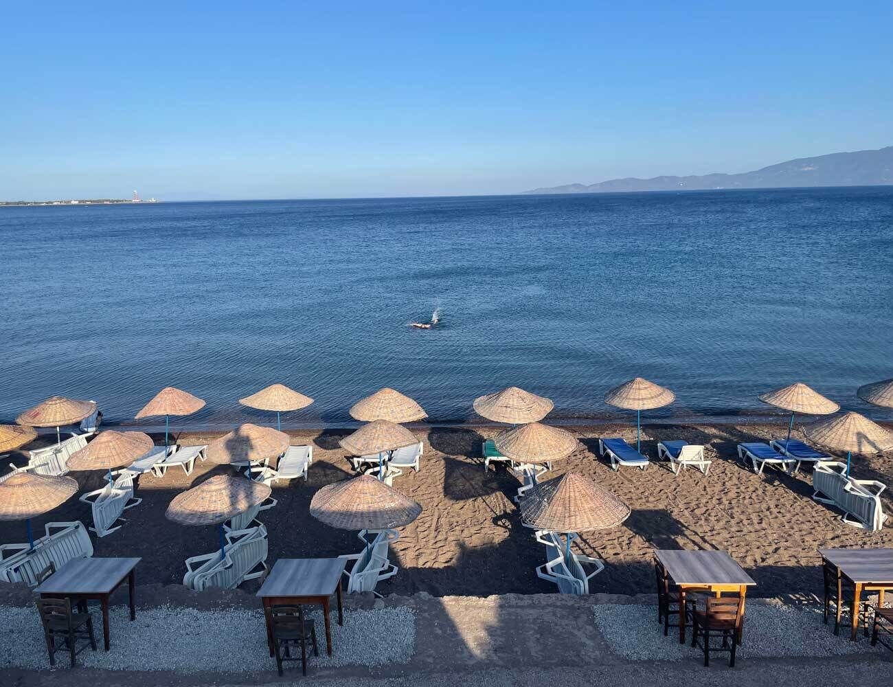 A beach with umbrellas and lounge chairs, a clear view of the sea, and a distant shoreline.