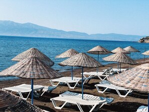 A beach with sun loungers and woven umbrellas.