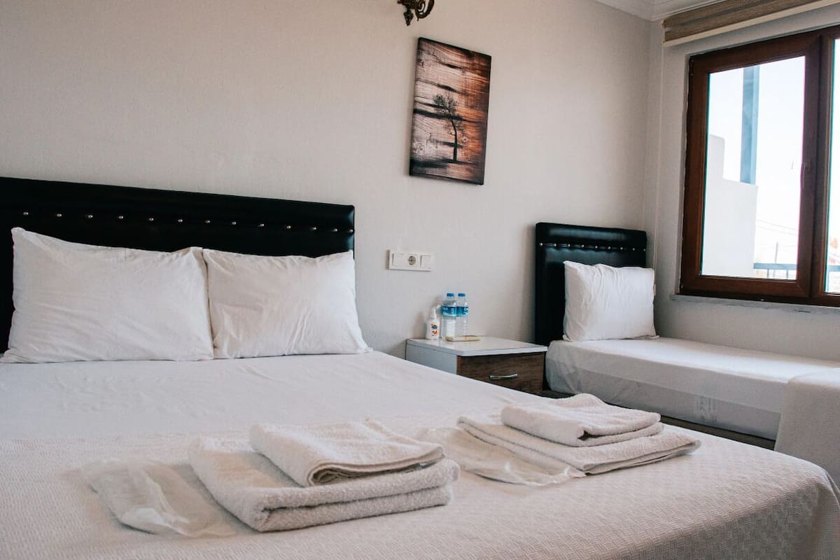 Una habitación de hotel con una cama, dos mesitas de noche, un ventanal y un cuadro en la pared.