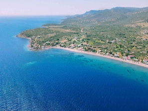 An aerial view of a coastal area with a beach, buildings, and green hills.