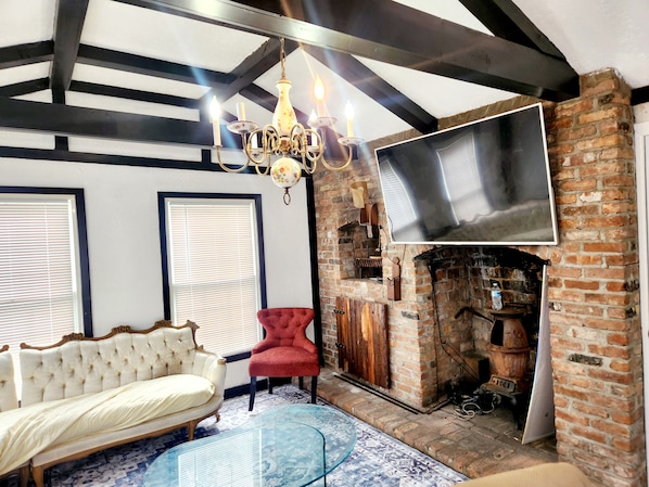 A room with a fireplace, a sofa, a red chair, a chandelier, and a large TV mounted on the wall.