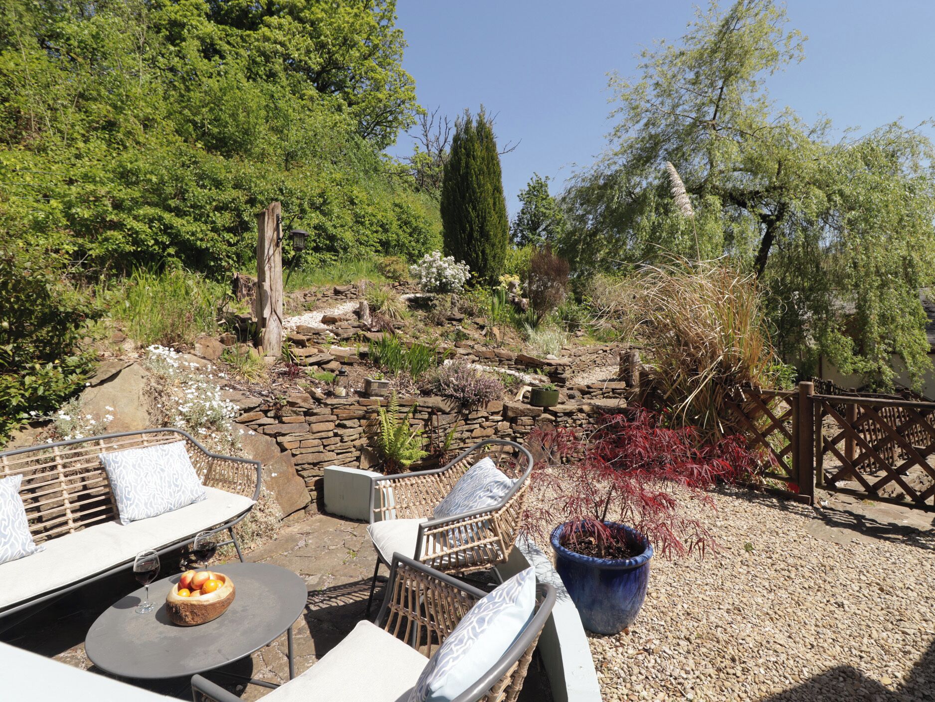 An outdoor seating area with stone walls, a variety of plants, and a wooden fence.
