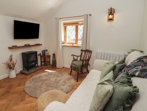 A cozy living room with a fireplace, a television, a window with curtains, a wooden chair, and a sofa with cushions.