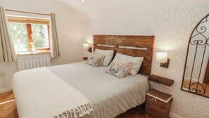 A bedroom with a wooden headboard, two bedside lamps, a bedside table, a wicker basket, and a window with curtains.