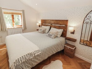 A bedroom with a wooden headboard, two bedside lamps, a bedside table, a wicker basket, and a window with curtains.