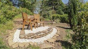 A garden with a stone pathway, wooden chairs, and surrounding greenery.