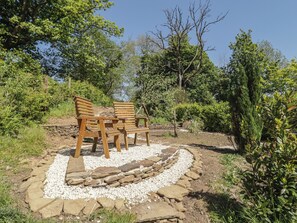 A garden with a stone pathway, wooden chairs, and surrounding greenery.