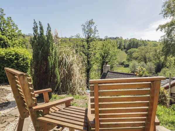 Two wooden chairs facing a view of a lush green landscape with trees and a building in the distance.