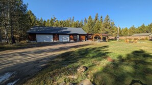 A two-story log cabin with a garage, a covered patio, and a fenced yard. - Stargazer Hideaway: Hot Tub, Outdoor Dinning, pet-friendly; close to Yellowstone (Island Park)