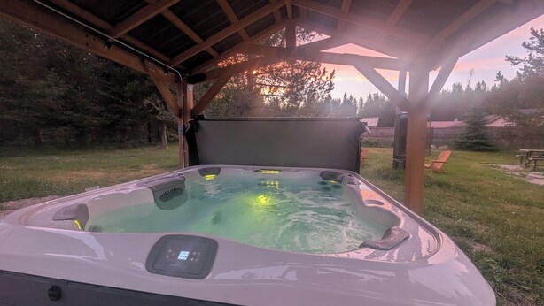 A hot tub under a wooden pergola with a grassy yard and trees in the background. - Stargazer Hideaway: Hot Tub, Outdoor Dinning, pet-friendly; close to Yellowstone (Island Park)