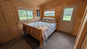 Une chambre à coucher aux murs lambrissés, avec un lit, deux fenêtres et une porte.