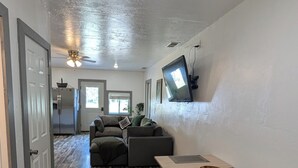 A spacious living area with a wooden floor, a flat-screen TV mounted on the wall, a ceiling fan, and a kitchen in the background. - Stargazer Hideaway: Hot Tub, Outdoor Dinning, pet-friendly; close to Yellowstone (Island Park)