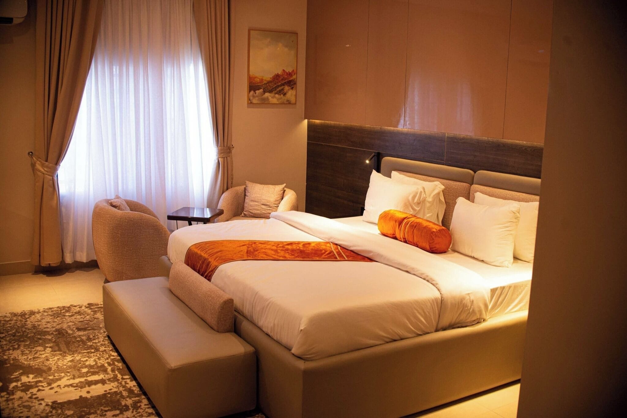 Habitación de hotel con una cama grande, un área de descanso con una silla, una mesita y un cuadro en la pared.