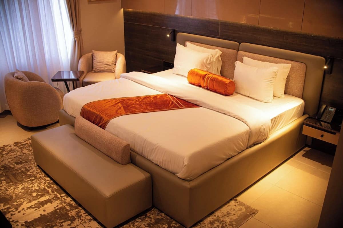 Una habitación de hotel moderna con una cama grande, un sofá, una mesita y una silla.