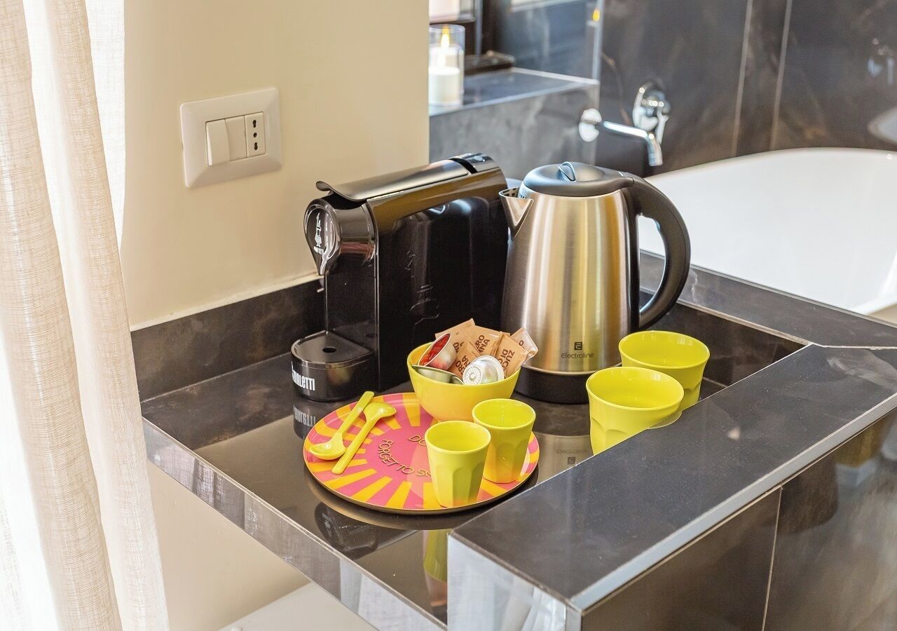Una encimera de cocina con una cafetera, un hervidor, un cuenco con monedas y tres tazas amarillas.