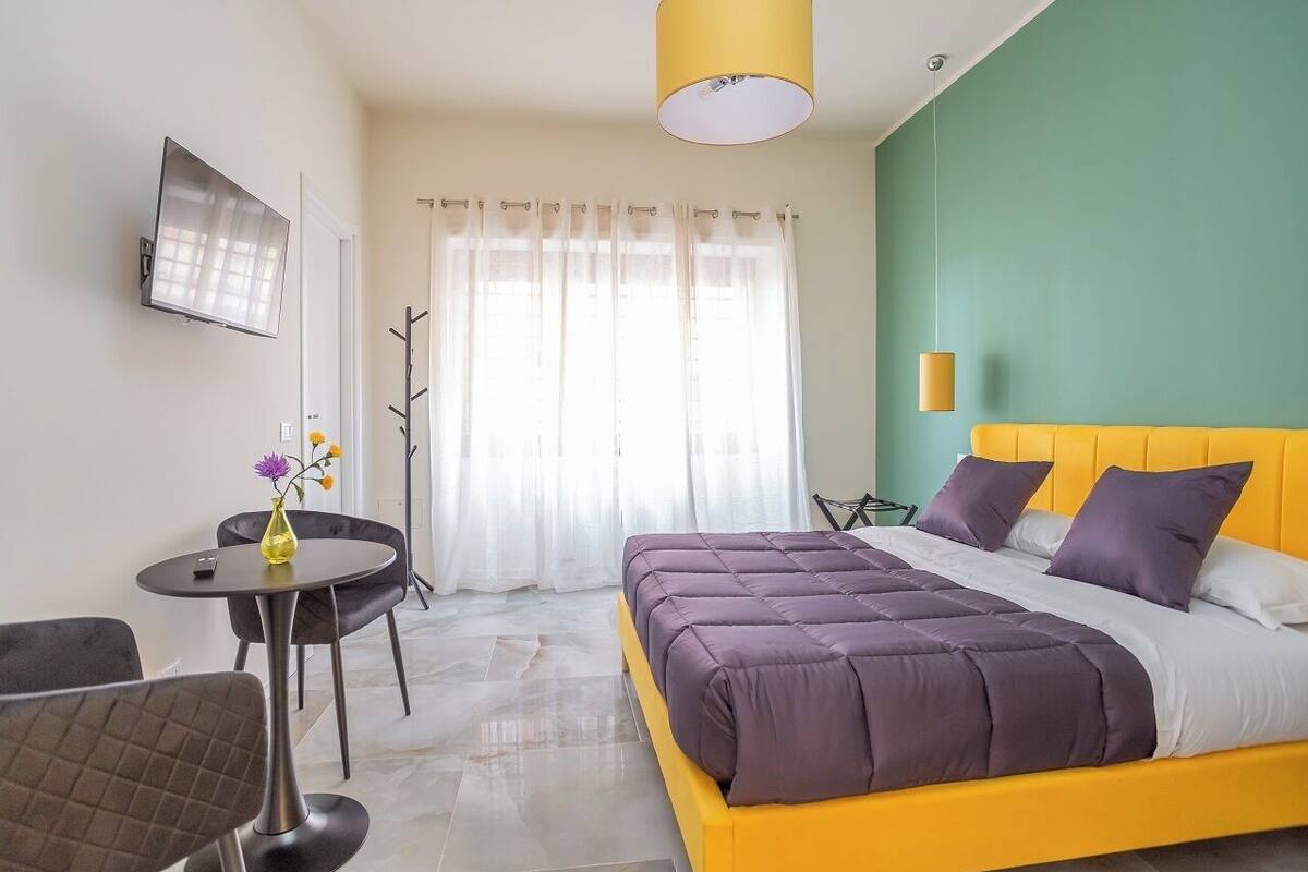 Una habitación de hotel con una cama, un televisor, una mesa con un florero y una silla.