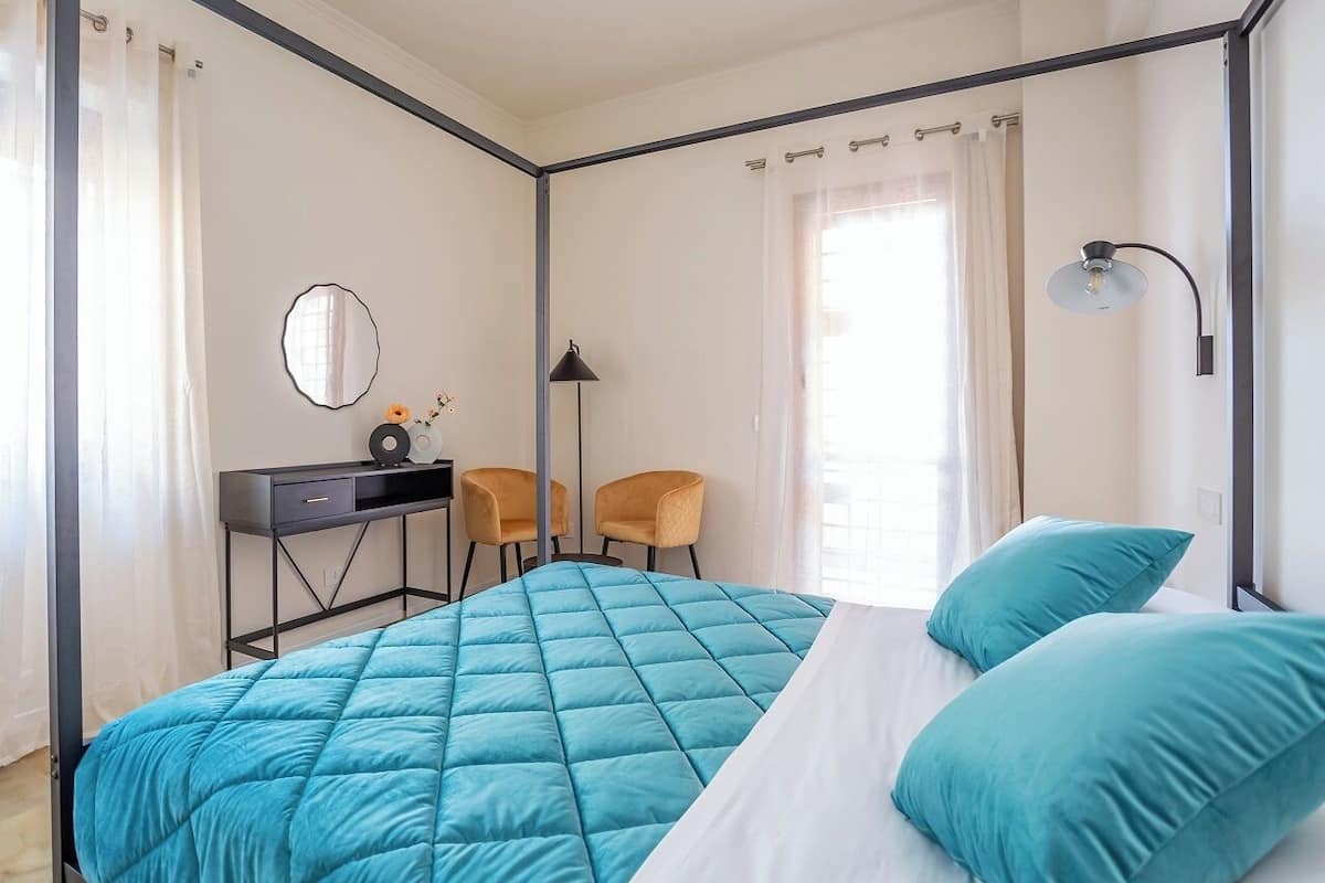 Un dormitorio con cama, escritorio, dos sillas, espejo y ventana con cortinas.