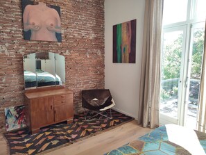 A bedroom with a brick wall, a wooden dresser, a mirror, a colorful rug, and a window with a view of greenery. - Large, luxurious family home in Haarlem, close to city, beach and Amsterdam. (Haarlem)
