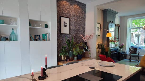 Ett modernt kök med en bänkskiva i marmor, en svart induktionshäll och ett rött ljus i en dekorativ ljusstake.